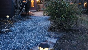 Une maison moderne avec un chemin de gravier menant à l’entrée, entourée d’arbres et dotée d’une terrasse en bois.