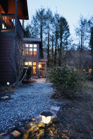 A modern house with a gravel pathway leading to the entrance, surrounded by trees and a wooden deck.
