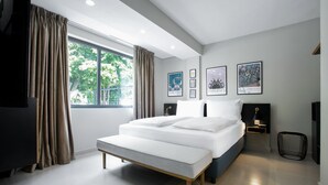 A modern bedroom with a large bed, a bench, and a view of greenery outside. - Nordic Hotel Lagos (Lagos)
