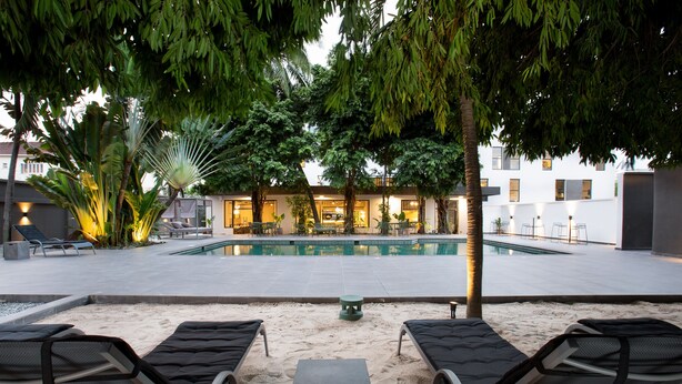 A poolside area with lounge chairs, a small table, and a building in the background. - Nordic Hotel Lagos (Lagos)