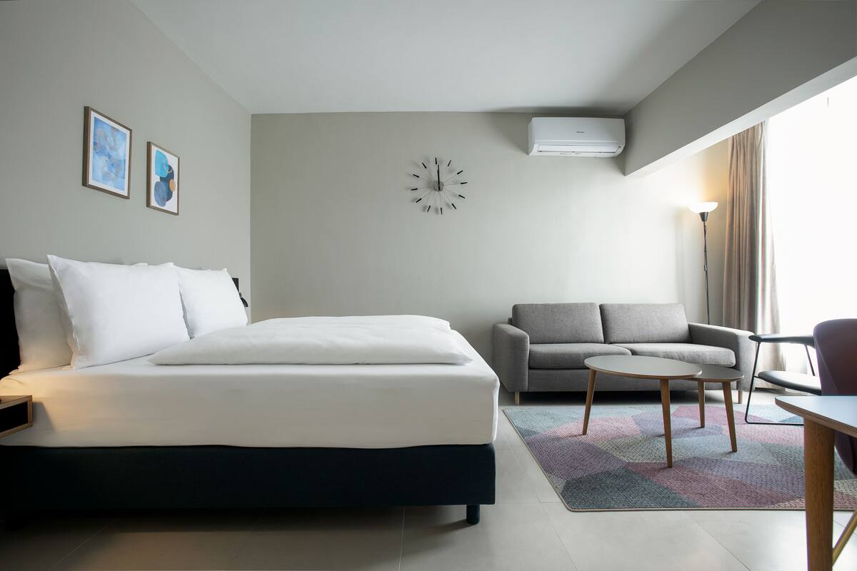 Quarto de hotel moderno com uma cama, um sofá, uma mesinha e um relógio na parede.