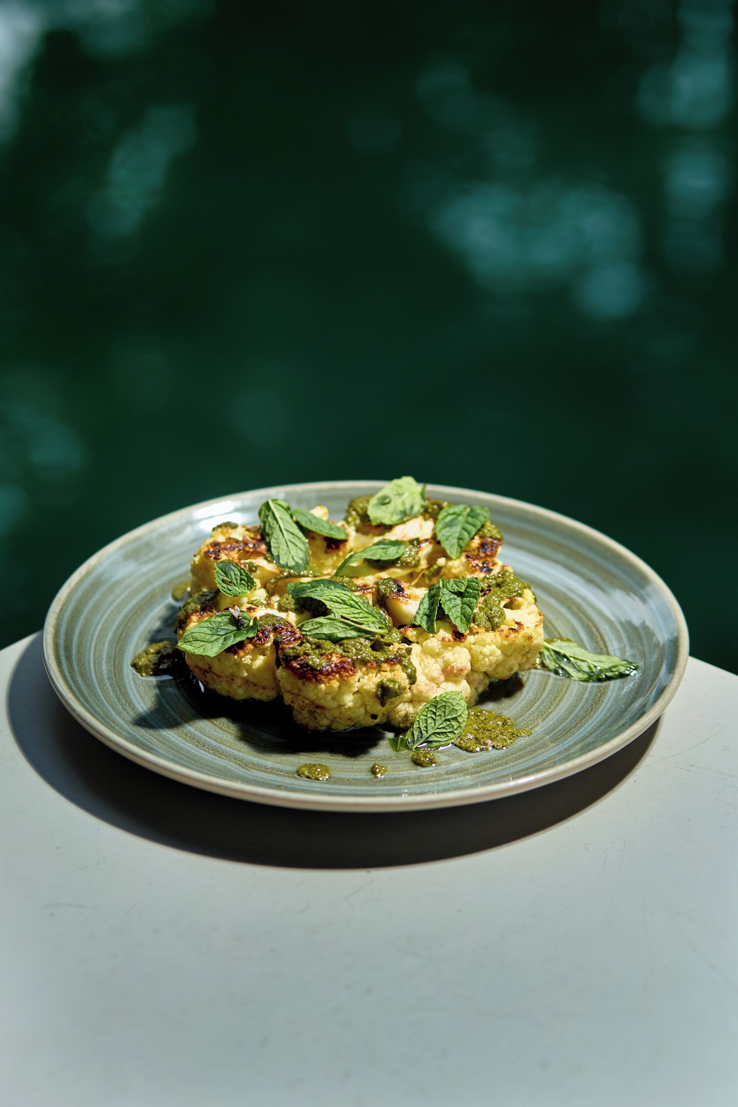 A plate of food with a green sauce and mint leaves on a ceramic plate.