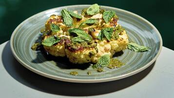 A plate of food with a green sauce and mint leaves on a ceramic plate.