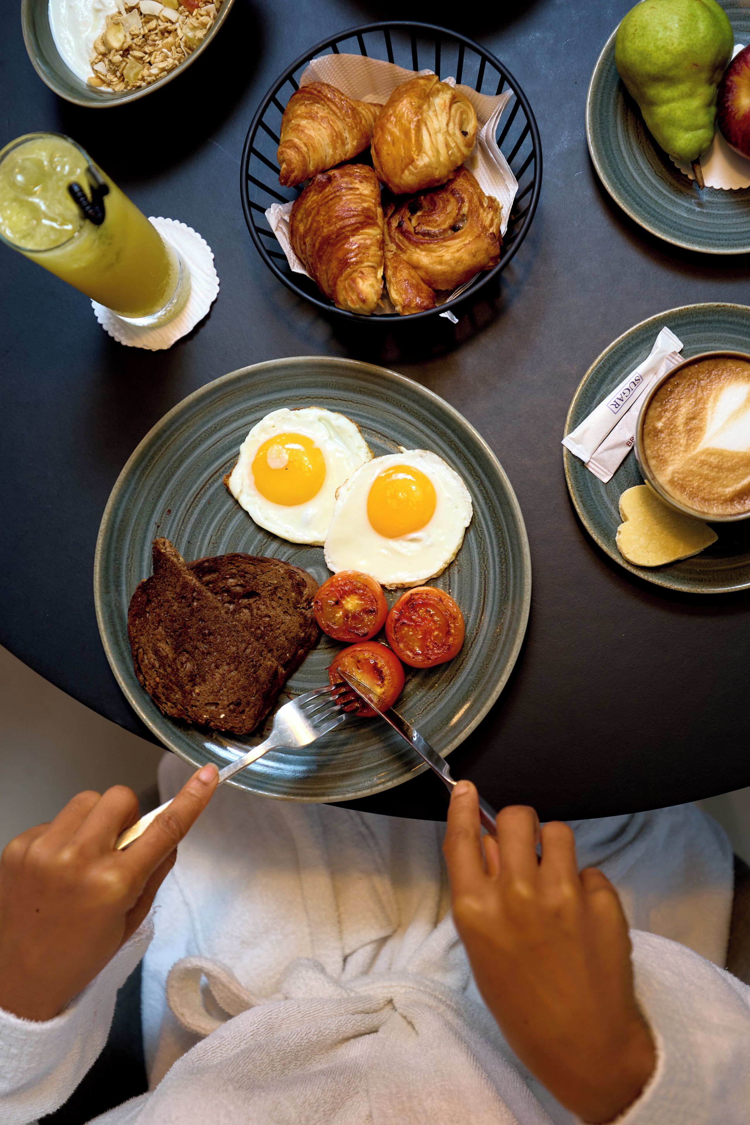 A breakfast setting with croissants, eggs, tomatoes, and toast on a plate.