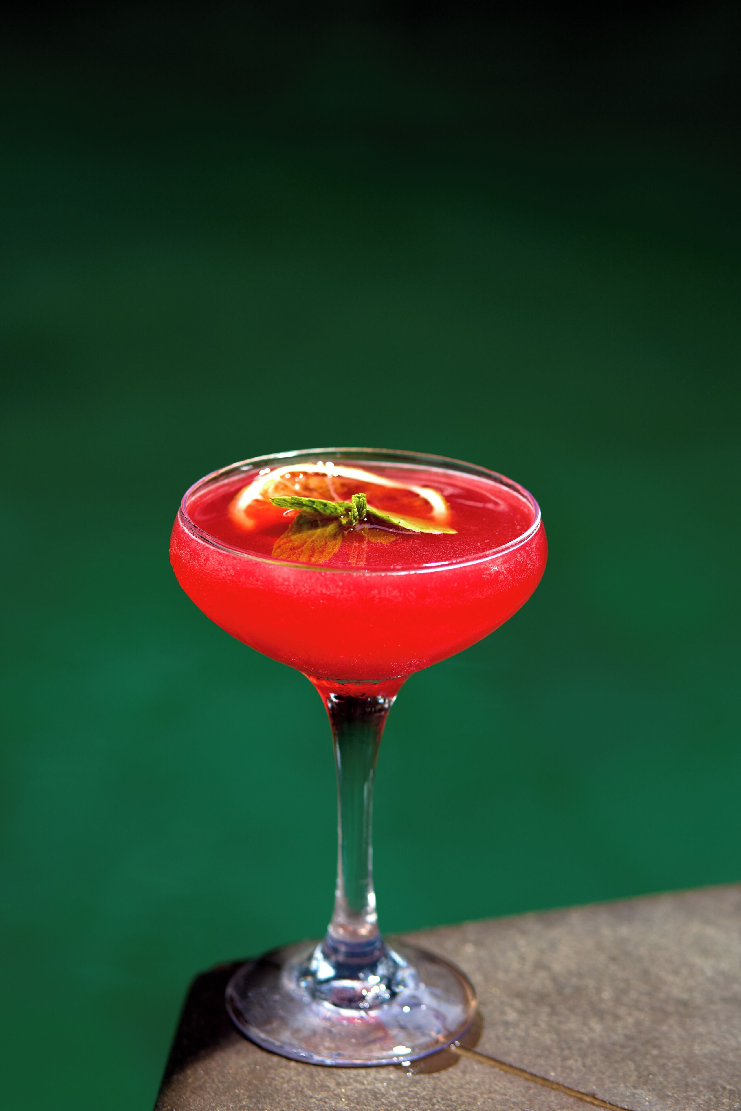 A cocktail in a stemmed glass with a garnish, set against a green background.