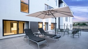 A modern outdoor patio with lounge chairs and a large umbrella, adjacent to a building with large windows and a visible bathroom. - Nordic Hotel Lagos (Lagos)