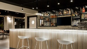 A bar area with a wooden counter, three white stools, and shelves of liquor bottles. - Nordic Hotel Lagos (Lagos)