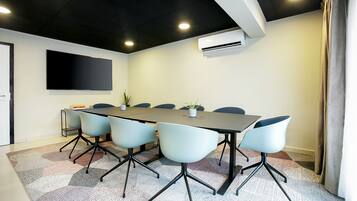 A conference room with a long table, six chairs, a flat-screen TV, and an air conditioning unit.