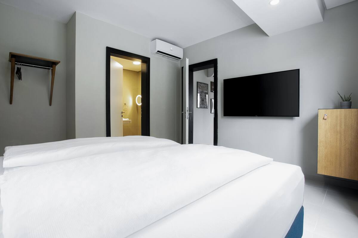 Quarto de hotel moderno com uma cama grande, uma televisão de tela plana na parede e um armário de madeira.