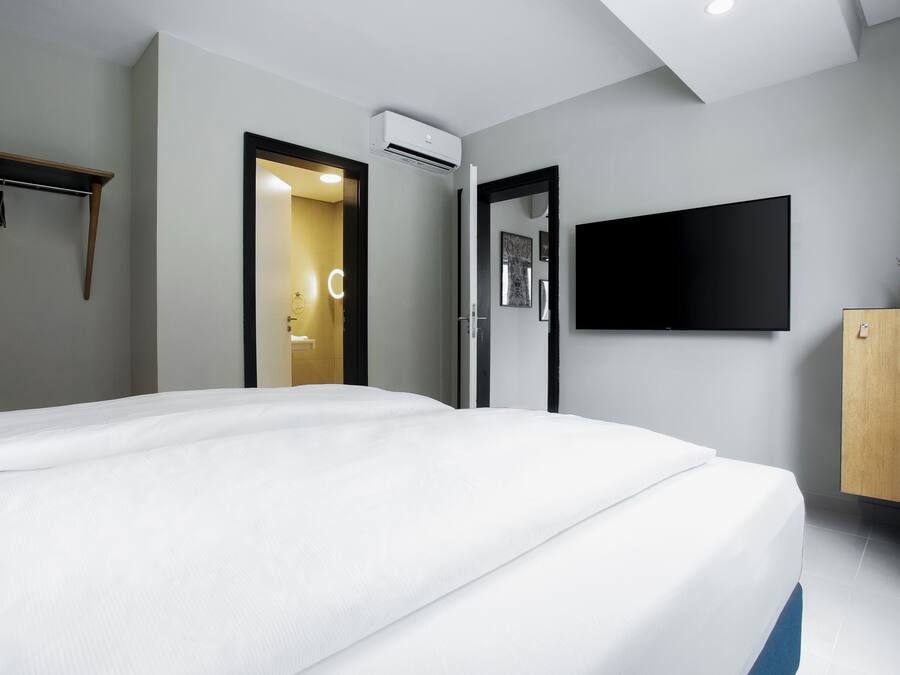 Une chambre d’hôtel moderne dotée d’un grand lit, d’un téléviseur à écran plat fixé au mur et d’une armoire en bois.
