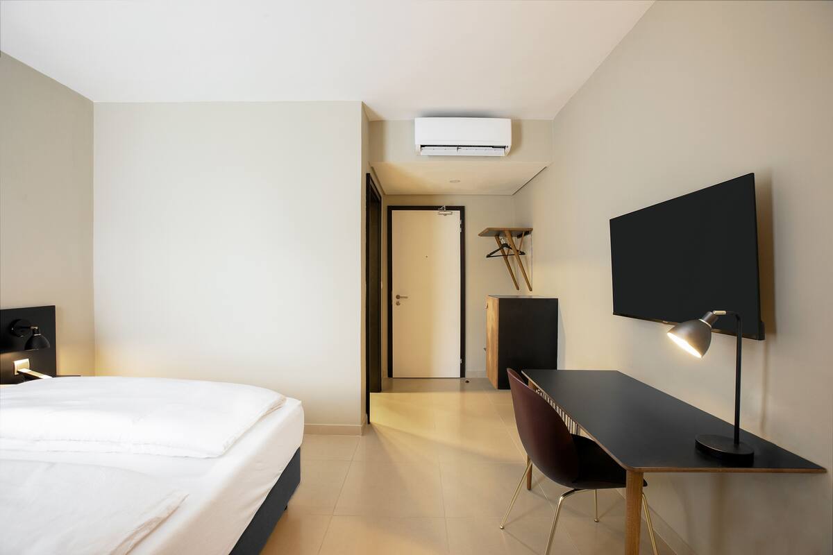 Quarto de hotel com cama, escrivaninha, cadeira, televisão de tela plana e ar condicionado.