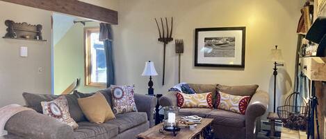 A cozy living room with two sofas, a coffee table, and a cowhide rug. There is a framed picture on the wall and a rustic lamp.