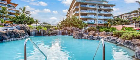 A swimming pool with a waterfall feature, surrounded by lush greenery and modern buildings.