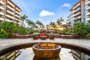 A resort pool area with a fire pit, outdoor seating, and palm trees.