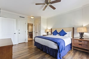 Quarto de hotel com cama, mesas de cabeceira, ventoinha no teto e porta que dá para outro quarto.