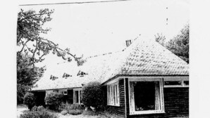 Ein zweistöckiges Holzhaus mit Satteldach und Veranda.
