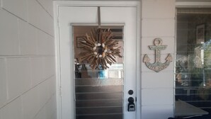 Uma porta branca com painel de vidro jateado, um letreiro decorativo de âncora e uma placa com a inscrição 'Pescaria'.