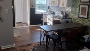 Cozinha moderna com armários brancos, sala de jantar com mesa e cadeiras, e um tapete estampado no chão.