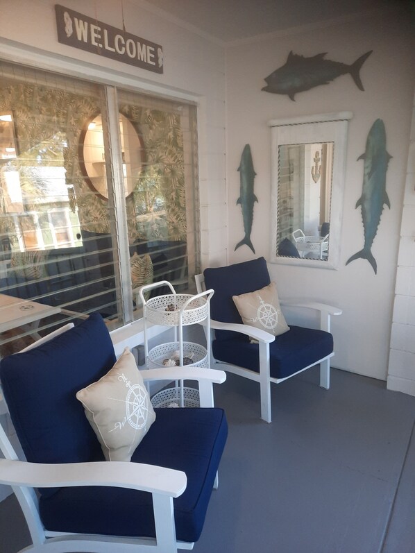A seating area with two white chairs and blue cushions, a welcome sign, and two large fish wall art pieces.