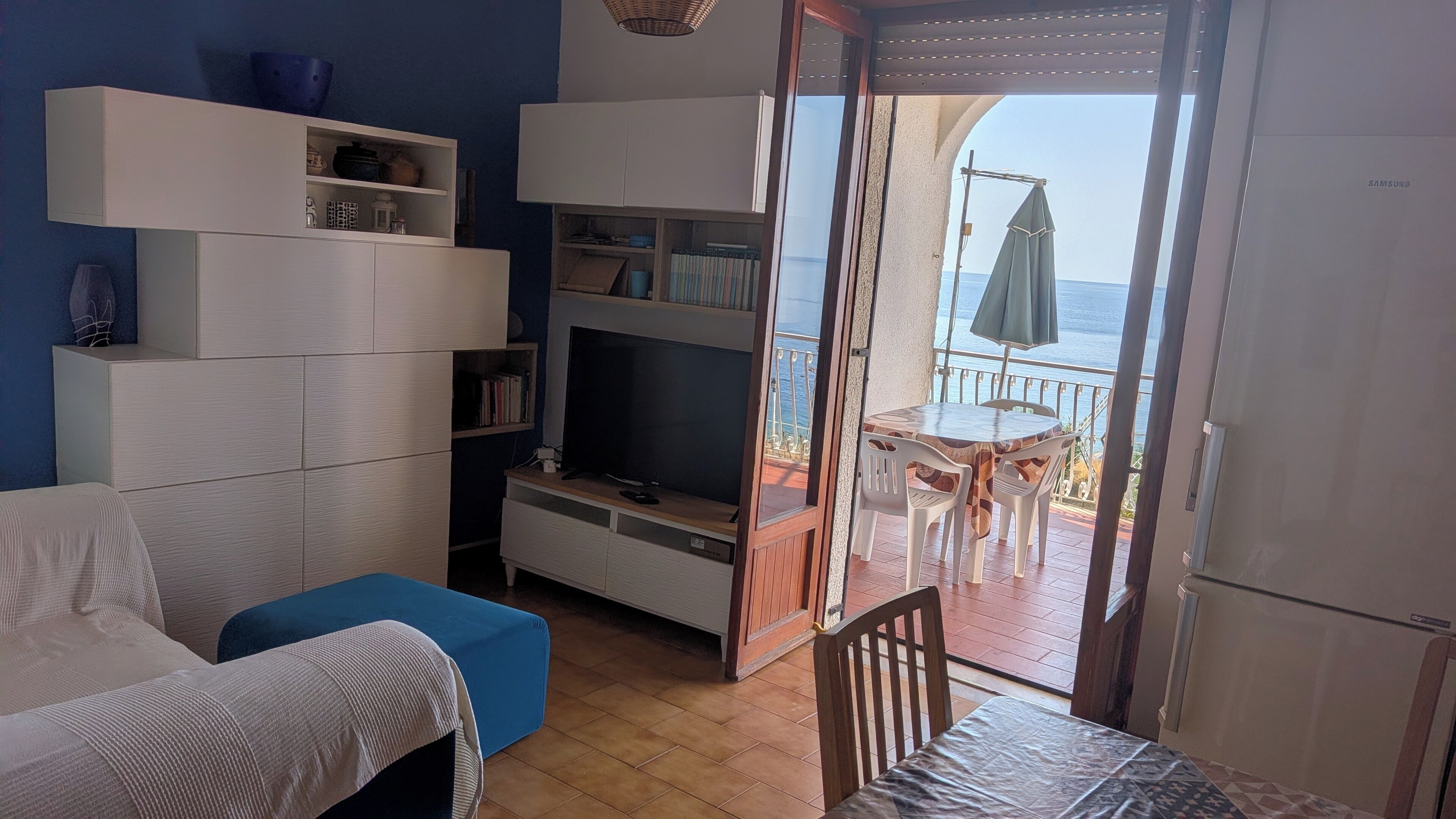 Un salon comprenant un canapé, un téléviseur et des étagères, qui donne sur un balcon avec une table et des chaises.