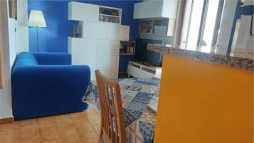 Uma sala de estar com um sofá azul, uma cadeira de madeira, uma televisão e uma estante de livros.