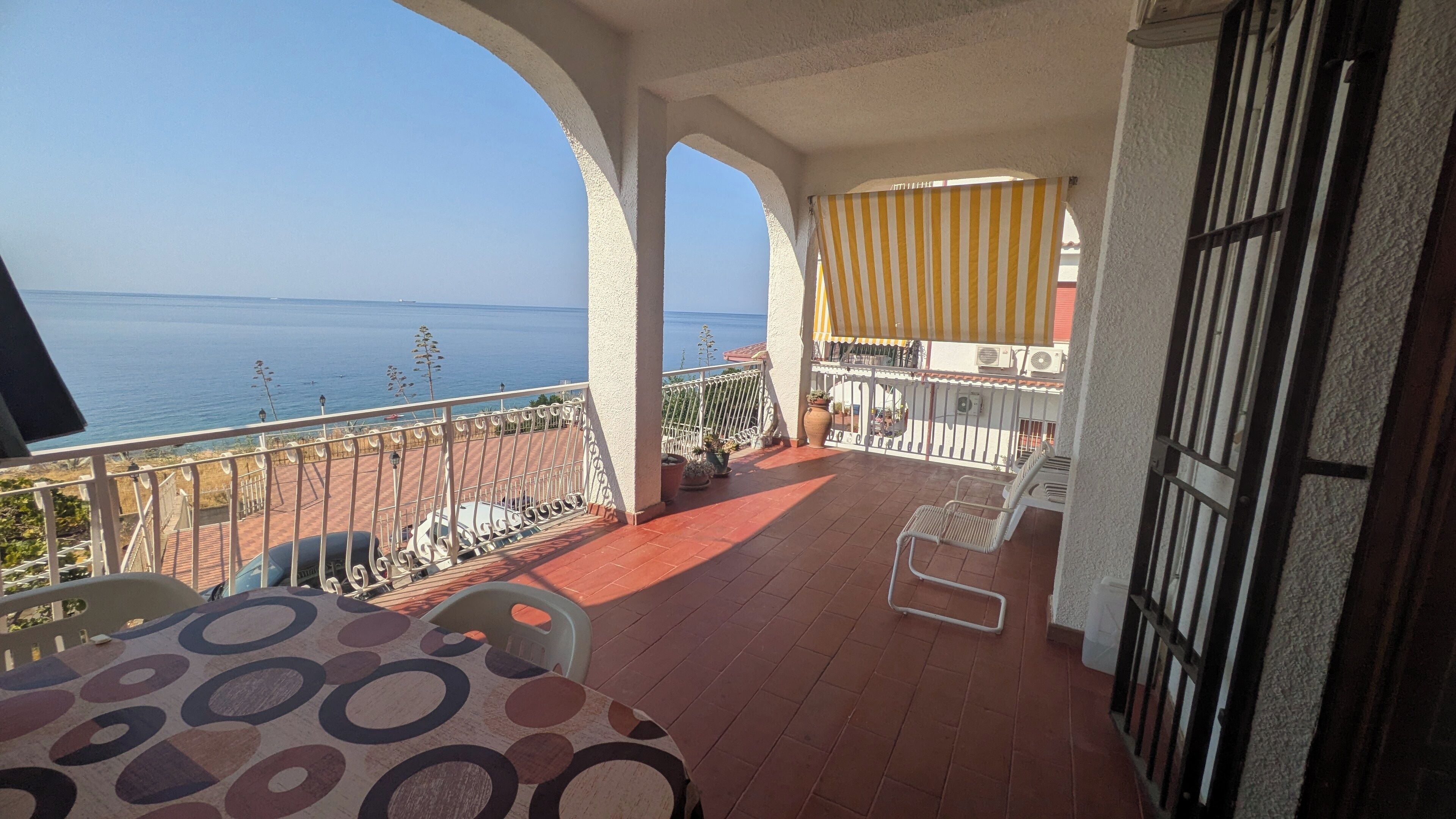Ein Balkon mit Meerblick, einem Tisch mit Stühlen und einem Streifen-Jalousie.