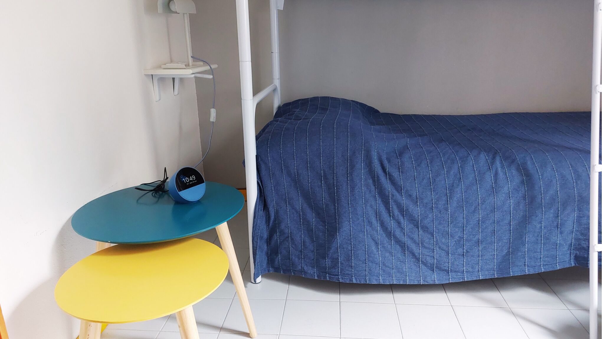 A small, single-bed room with a bunk bed, a desk with a chair, and a bedside table.