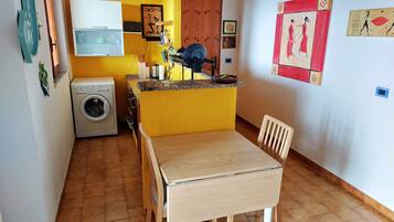 A compact kitchen with a washing machine, a microwave, and a small dining area with a wooden table and chair.