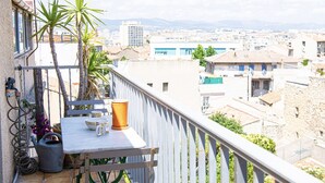 Een balkon met een tafel, stoelen, een bloempot en uitzicht op een stadsgezicht.
