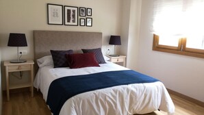 Un dormitorio ordenado con cama, dos mesitas de noche, una ventana con persianas e imágenes enmarcadas en la pared.