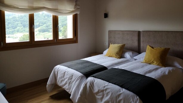 Un dormitorio con dos camas, un ventanal con vistas a la vegetación y techo de madera.