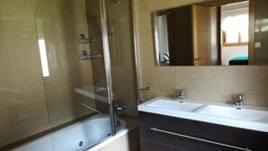 Un baño con ducha acristalada, bañera blanca y tocador con dos lavamanos y un espejo.