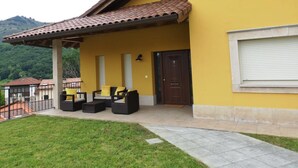 Un edificio amarillo con techo de tejas, un porche cubierto con mobiliario exterior y una puerta con ventana en la parte superior.