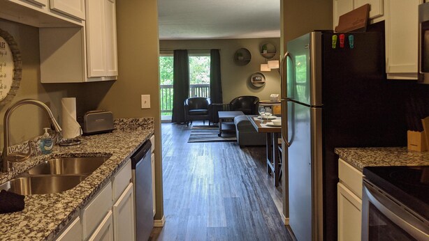 A kitchen with granite countertops, white cabinets, a stainless steel sink, a dishwasher, and a refrigerator. - Lee's Lane (Branson)