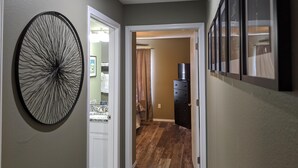 A hallway with a circular wall art, a door leading to a bathroom, and a dresser with a television. - Lee's Lane (Branson)