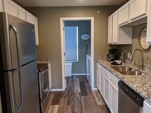 A modern kitchen with stainless steel appliances, a granite countertop, and a dishwasher. - Lee's Lane (Branson)