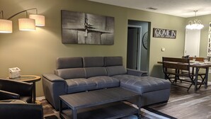 A modern living room with a sectional sofa, a coffee table, and a dining area with a bench and table. - Lee's Lane (Branson)