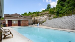 A swimming pool with a brick building, a stone retaining wall, and a grassy hill in the background. - Lee's Lane (Branson)