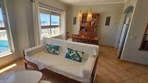 Ein Wohnzimmer mit Sofa, Esstisch und Blick auf Gebäude durch ein Fenster.