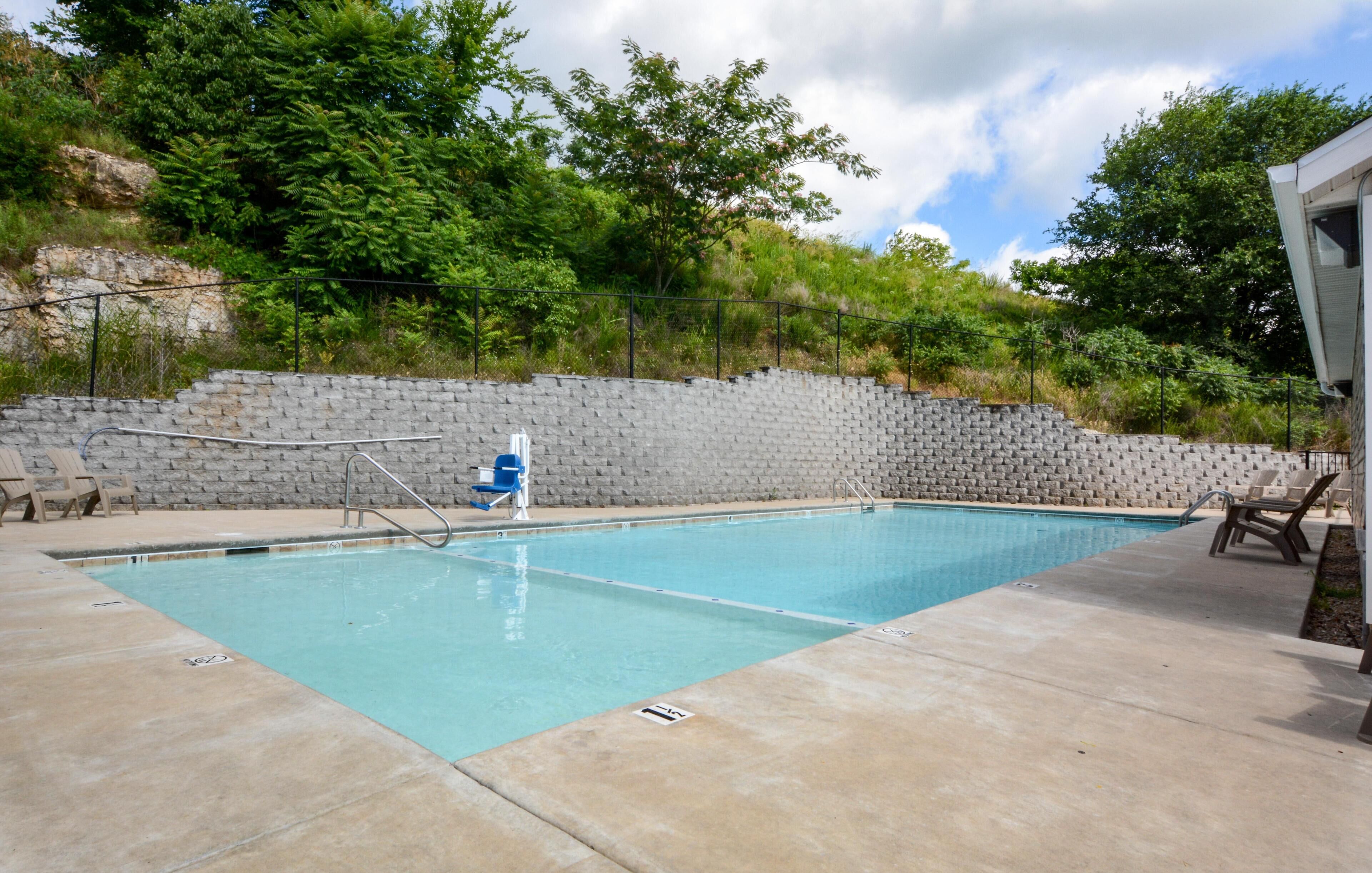 Una piscina rectangular con un muro de piedra y una valla metálica.