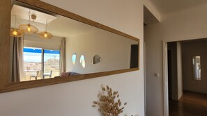 A hallway with a large mirror reflecting a balcony with a view of the sea.
