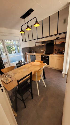 A modern kitchen with a dining area, featuring a large wooden table, black chairs, and pendant lighting. - Sea view AJACCIO gulf, hyper center, private parking, elevator, fiber. (Ajaccio)