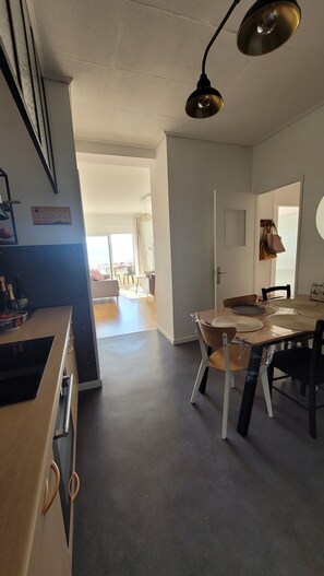 Ampla sala de estar com mesa de jantar, cadeiras e cozinha com pia e bancada.