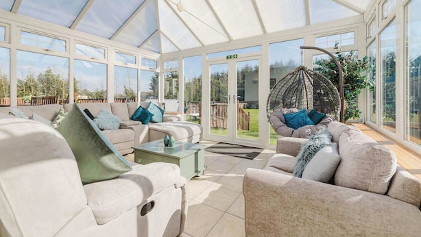 A conservatory with a glass ceiling, cushioned seating, and a hanging chair. - Greenknowes Farmhouse with Hot Tub and Bar (Blairadam)