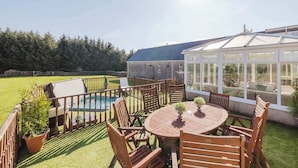 A backyard with a pool, wooden deck, and a conservatory. - Greenknowes Farmhouse with Hot Tub and Bar (Blairadam)