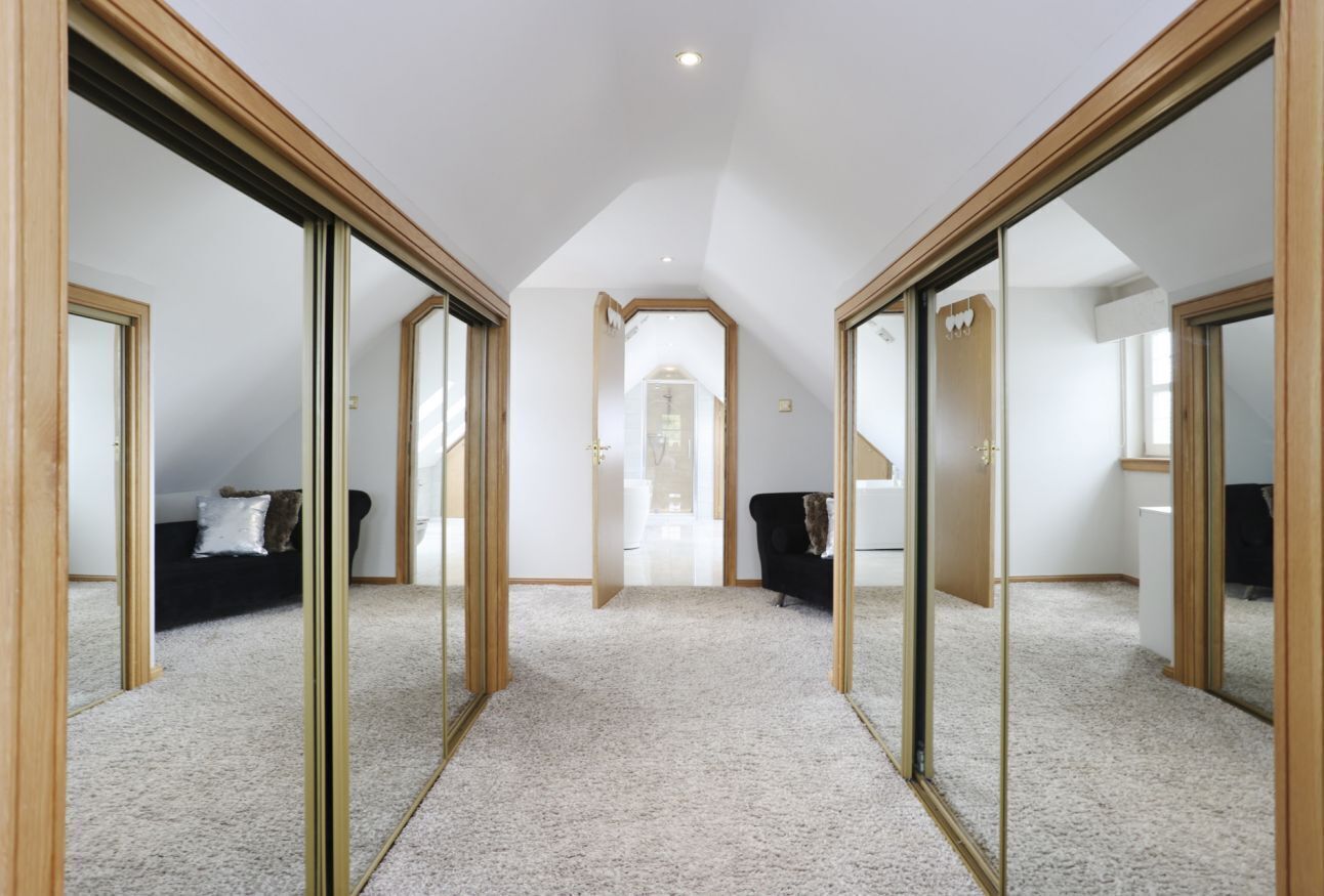 A hallway with mirrored walls, a carpeted floor, and a ceiling with recessed lighting.
