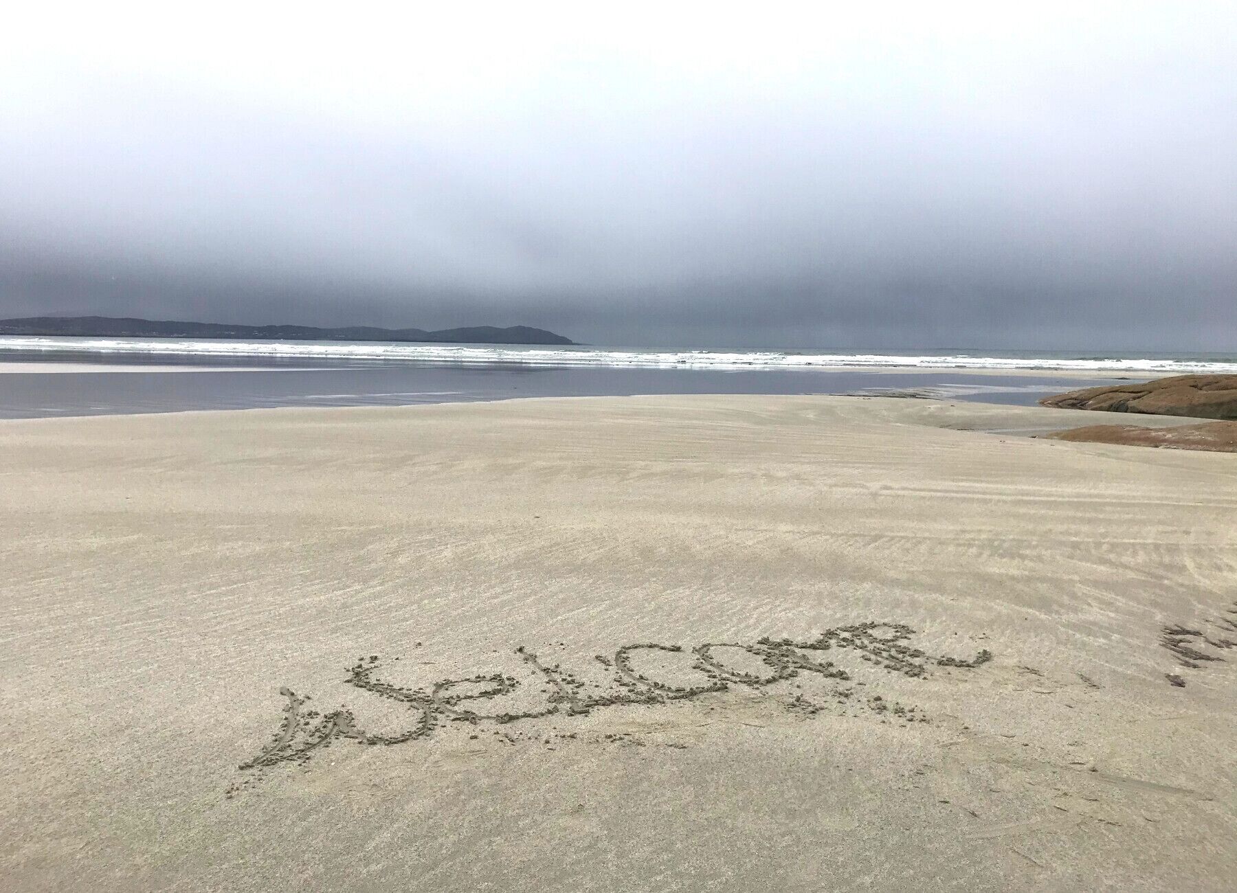 A beach with the word "welcome" written in the sand.