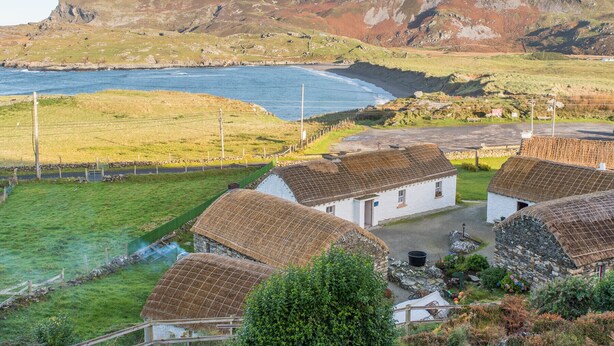 Uma vila costeira com casas de pedra tradicionais, uma encosta rochosa e vista para o mar.