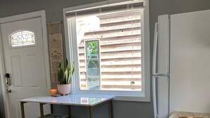 A kitchen with a wooden table, two stools, a window with blinds, a refrigerator, and a stainless steel sink. - East Main Downtown Bungalow  (Ashland)