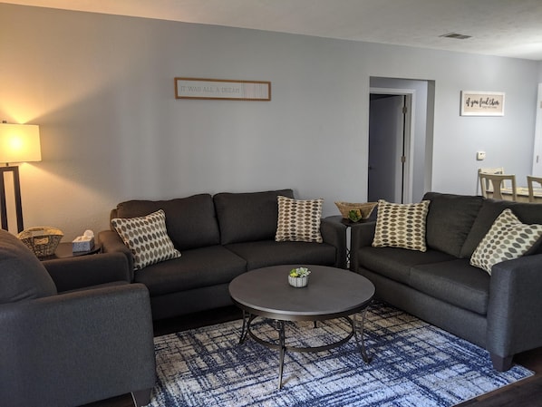A modern living room with a dark grey sectional sofa, a round coffee table, and a patterned rug.